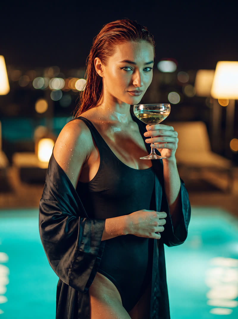 Yasmin wet-haired in a silk robe with a champagne coupe, night city behind